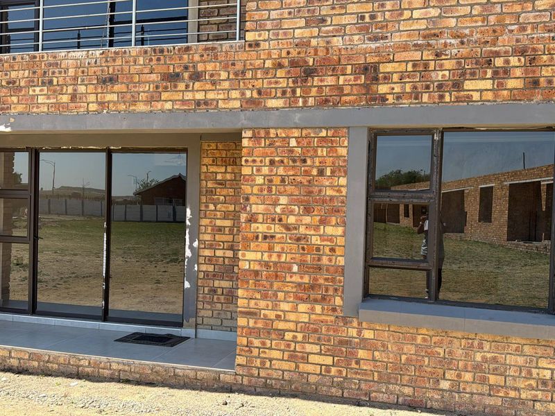 Rear exterior view of a face brick apartment building featuring a tiled patio, sliding glass doors, and aluminium window frames.