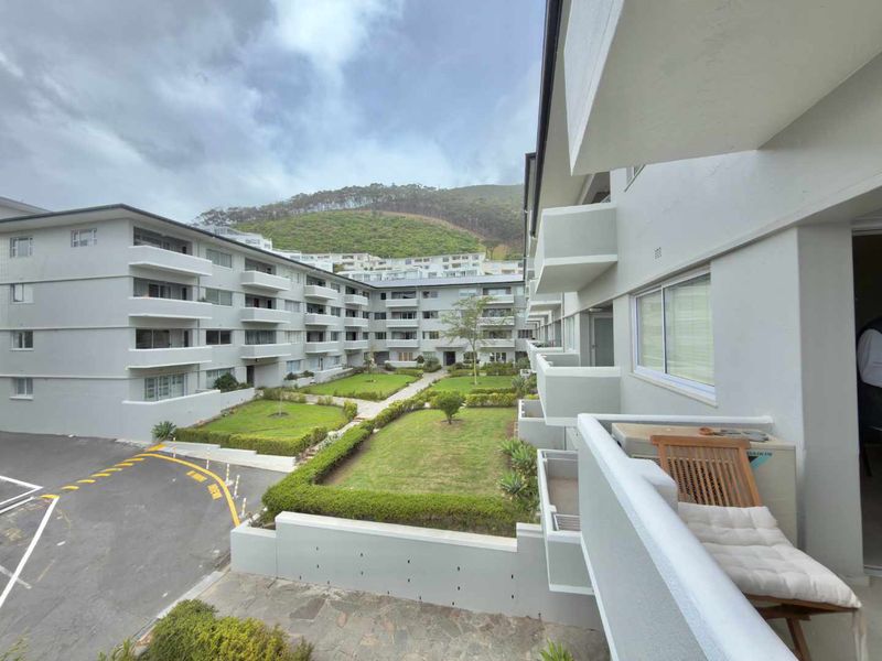 A view from a balcony overlooking a well-maintained apartment complex courtyard with landscaped gardens and paved driveway areas.