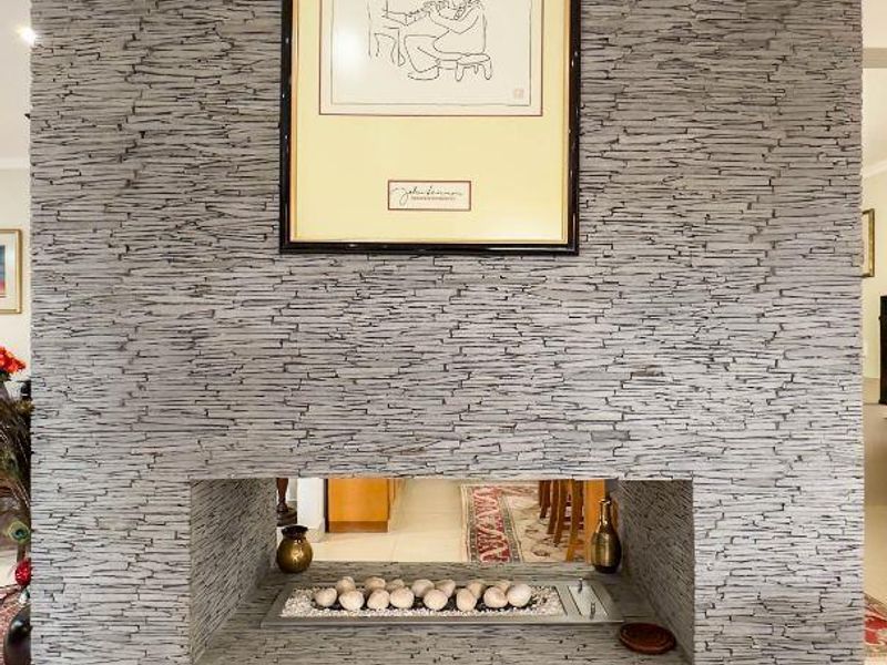 A modern living room feature wall finished in grey stacked stone with a built-in gas fireplace and neutral floor tiles.