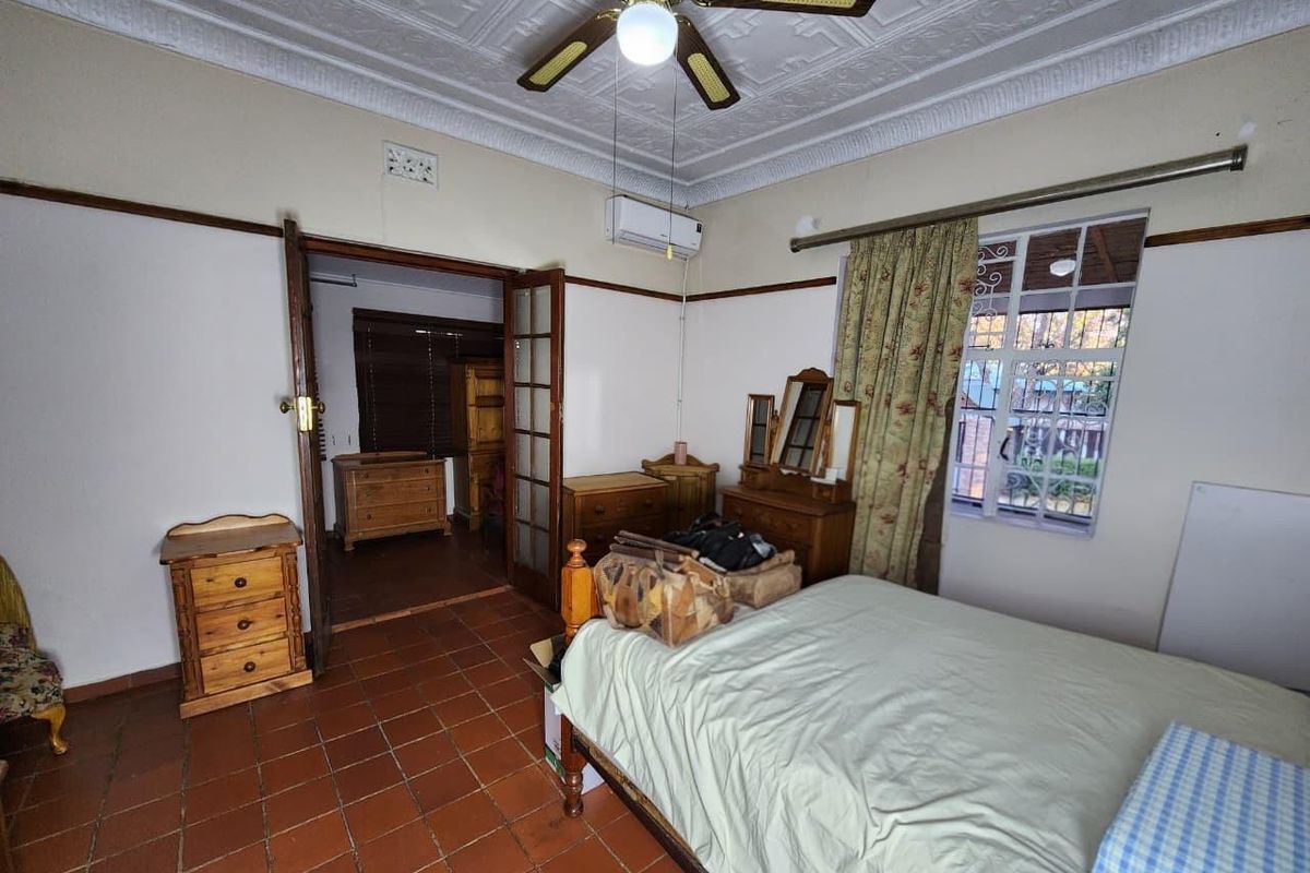 A bedroom featuring terracotta tile flooring, a decorative pressed metal ceiling, a ceiling fan, and a wall-mounted air conditioning unit.