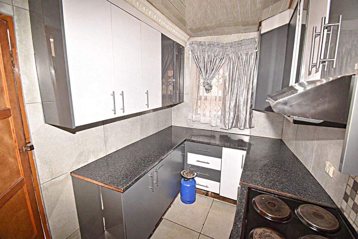 Compact kitchen featuring modern two-tone cabinetry, granite countertops, built-in electric hob with extractor fan, and neutral wall and floor tiling.