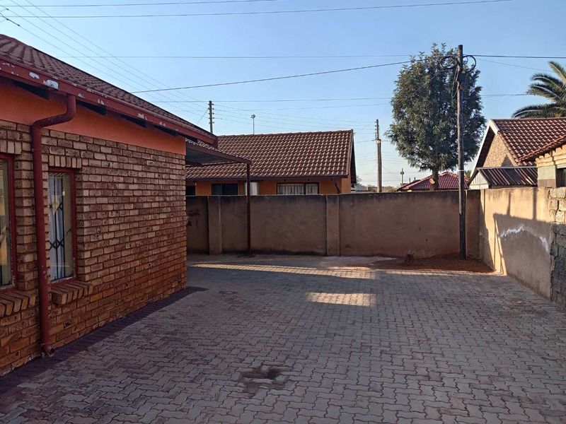 A rear exterior view of the property featuring a brick facade, paved courtyard area, and a solid perimeter wall.