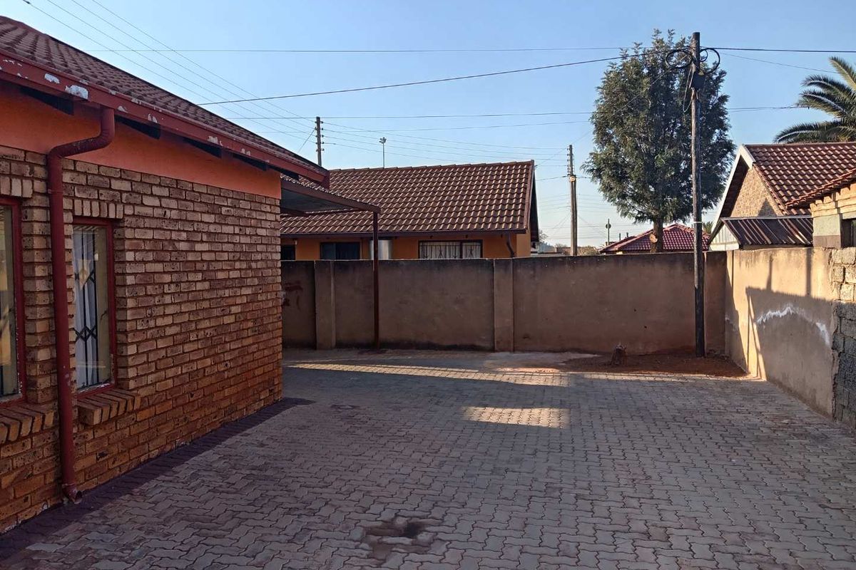 A rear exterior view of the property featuring a brick facade, paved courtyard area, and a solid perimeter wall.