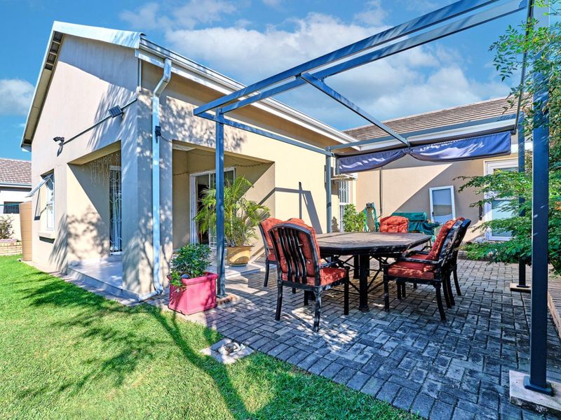 A paved outdoor patio area featuring a metal pergola structure, providing a functional space for outdoor dining and relaxation adjacent to the home.