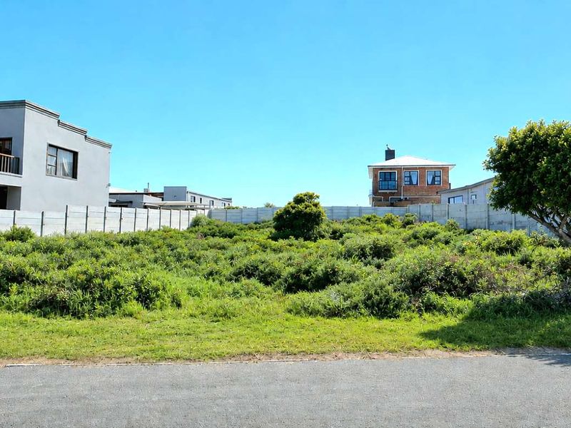 A vacant residential plot featuring a level grassed surface, enclosed by precast concrete boundary walls, with direct access to an asphalt road.