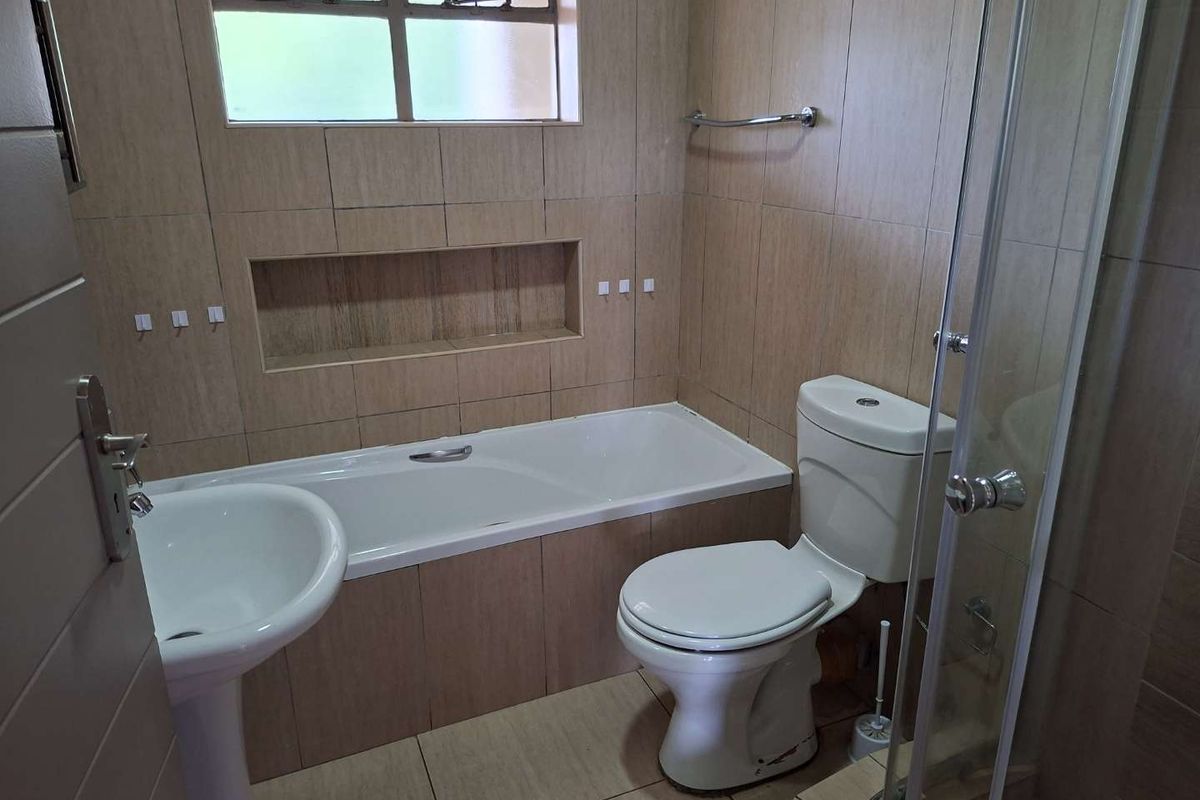 A functional bathroom featuring a pedestal basin, a built-in bathtub with a tiled niche, a toilet, and a separate glass-enclosed shower.