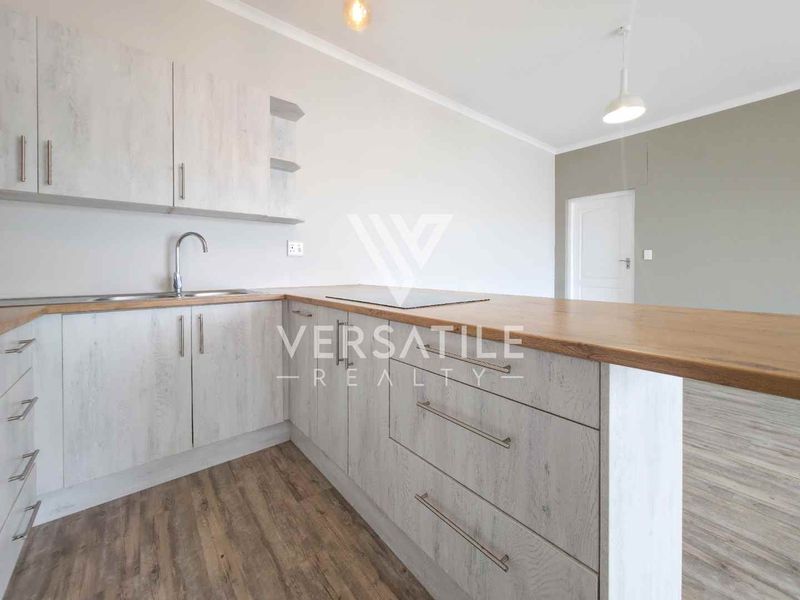 A modern, empty kitchen featuring light wood-grain cabinetry, a spacious laminate countertop, and durable laminate flooring, offering a clean and functional workspace.