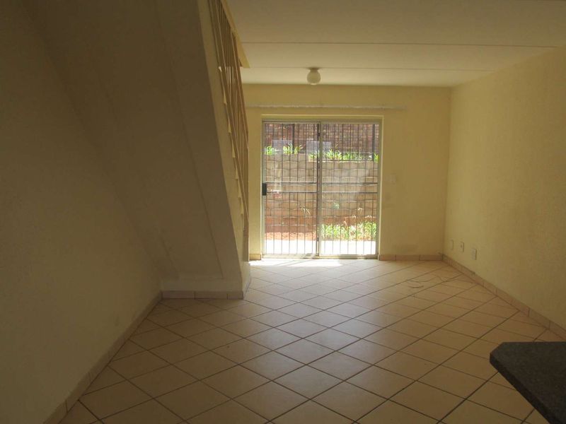 An empty living area featuring tiled flooring, a staircase, and a sliding glass door leading to an outdoor space.
