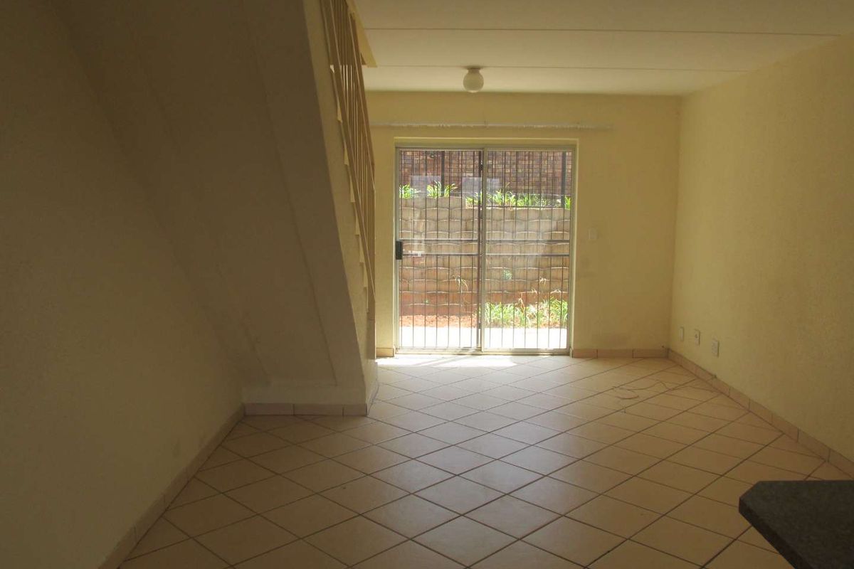 An empty living area featuring tiled flooring, a staircase, and a sliding glass door leading to an outdoor space.