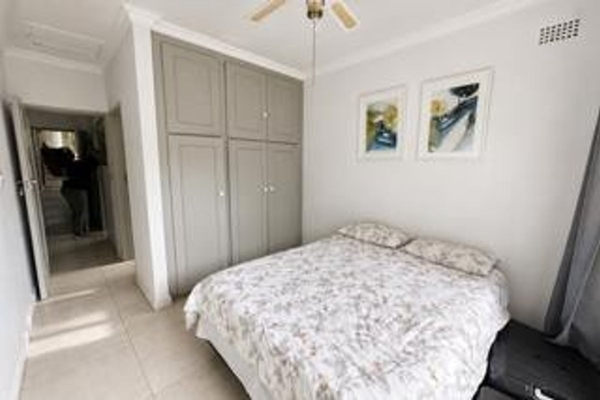 A well-maintained bedroom featuring neutral tiled flooring, built-in cupboards, and a ceiling fan, offering a clean and functional living space.
