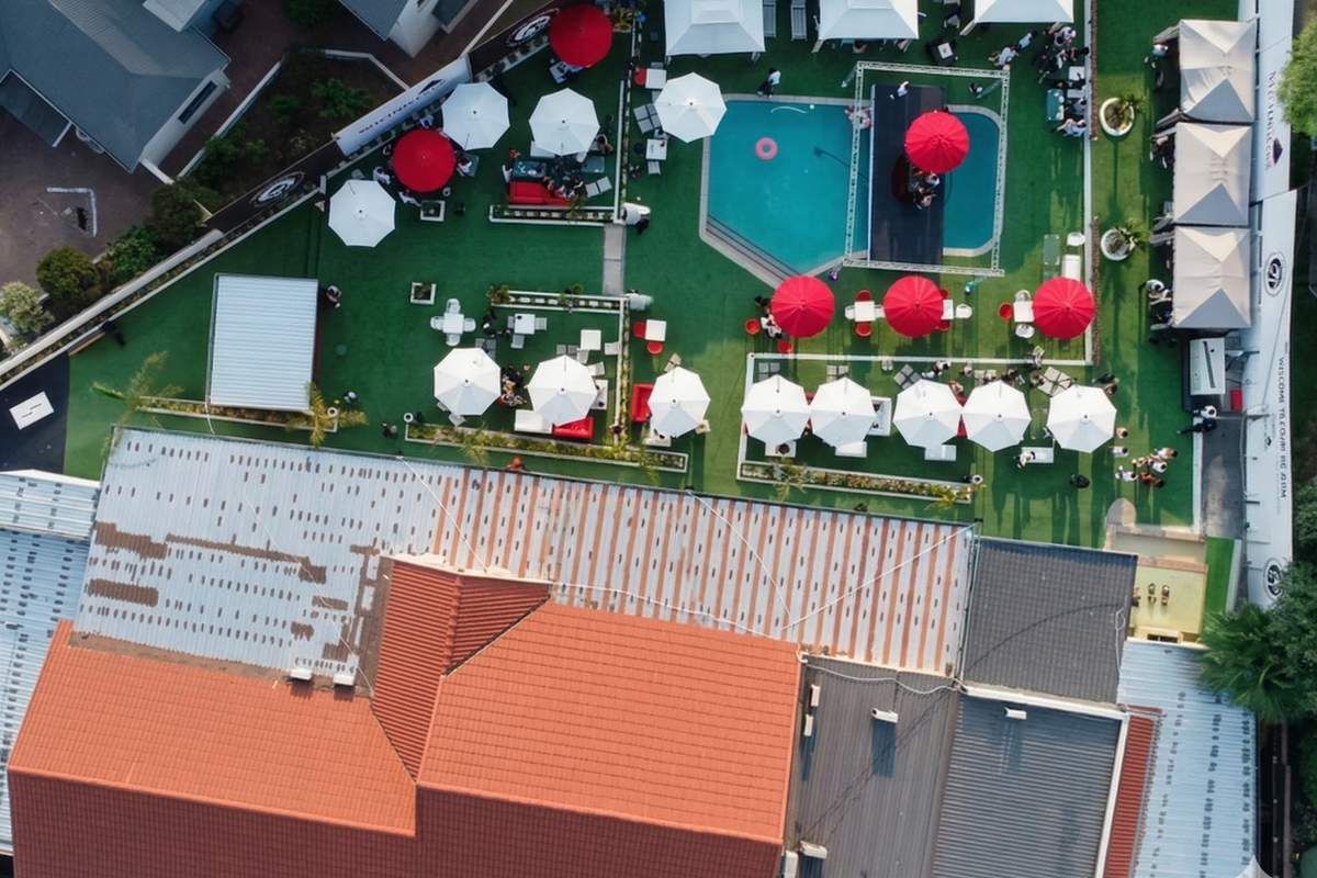 Aerial view of a mixed-use property featuring a swimming pool, outdoor entertainment area with multiple umbrellas, and a combination of tiled and metal roofing.