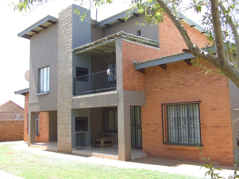 Rear view of a double-storey apartment featuring exposed brickwork, a stone-clad feature pillar, a covered patio with built-in braai, and an upper-level balcony.
