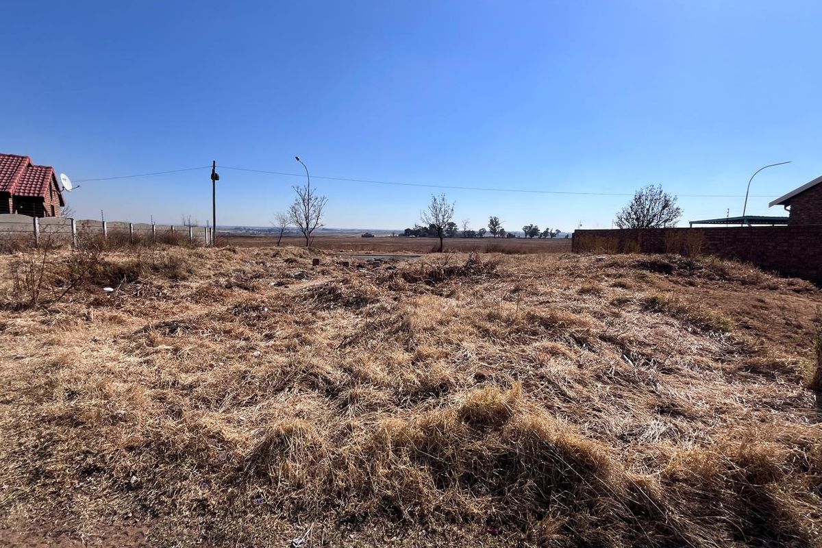 A vacant residential plot featuring dry, overgrown grass and perimeter boundary walls, offering an open landscape view.