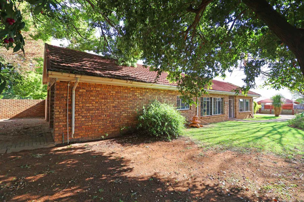 Rear view of a face brick house featuring a tiled roof, security gate, and surrounding garden area with a paved driveway.