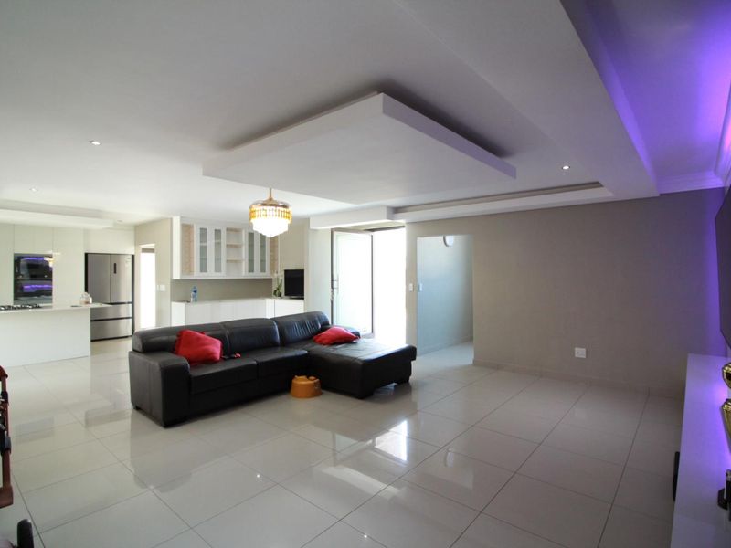 Spacious open-plan living area featuring modern porcelain tiling, a recessed ceiling with downlights, and a sleek, integrated kitchen with ample cabinetry.