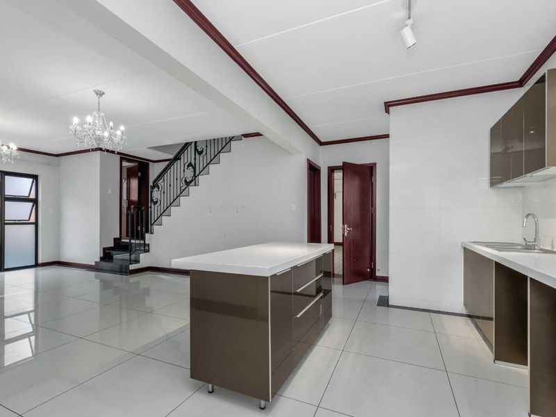 Spacious open-plan living and kitchen area featuring modern high-gloss cabinetry, a central island, tiled flooring, and a staircase with decorative wrought iron railings.