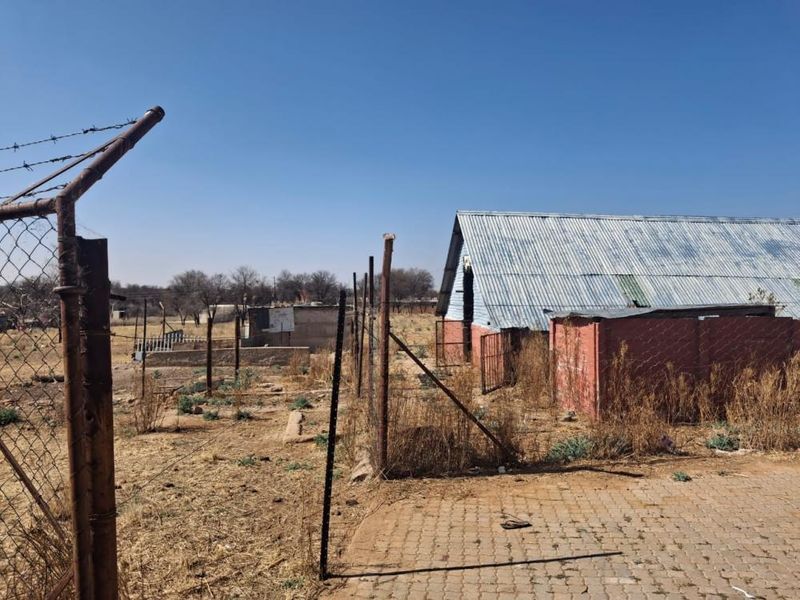 Rear view of the small holding property featuring corrugated iron structures, perimeter wire fencing, and paved areas in need of maintenance.