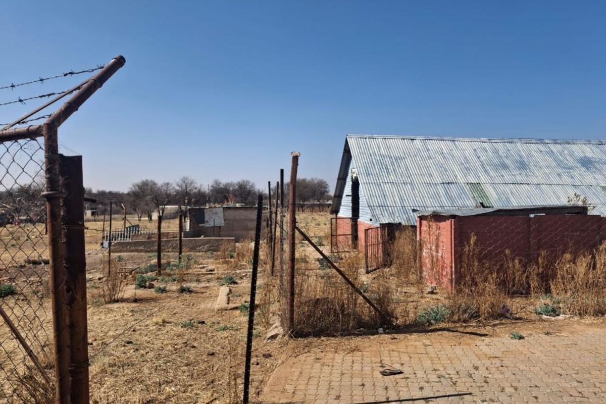 Rear view of the small holding property featuring corrugated iron structures, perimeter wire fencing, and paved areas in need of maintenance.