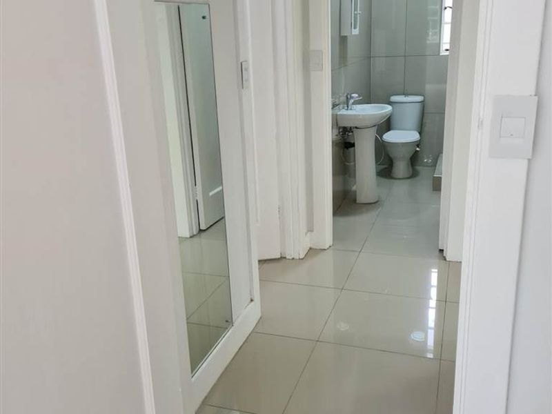 A clean, tiled hallway leading into a bathroom featuring a pedestal basin and toilet, with a built-in cupboard visible on the side.