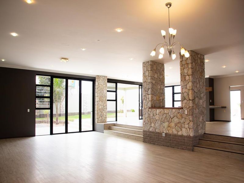 Spacious open-plan living area featuring stone-clad pillars, multi-level flooring, and large black-framed sliding doors providing seamless access to the outdoor space.