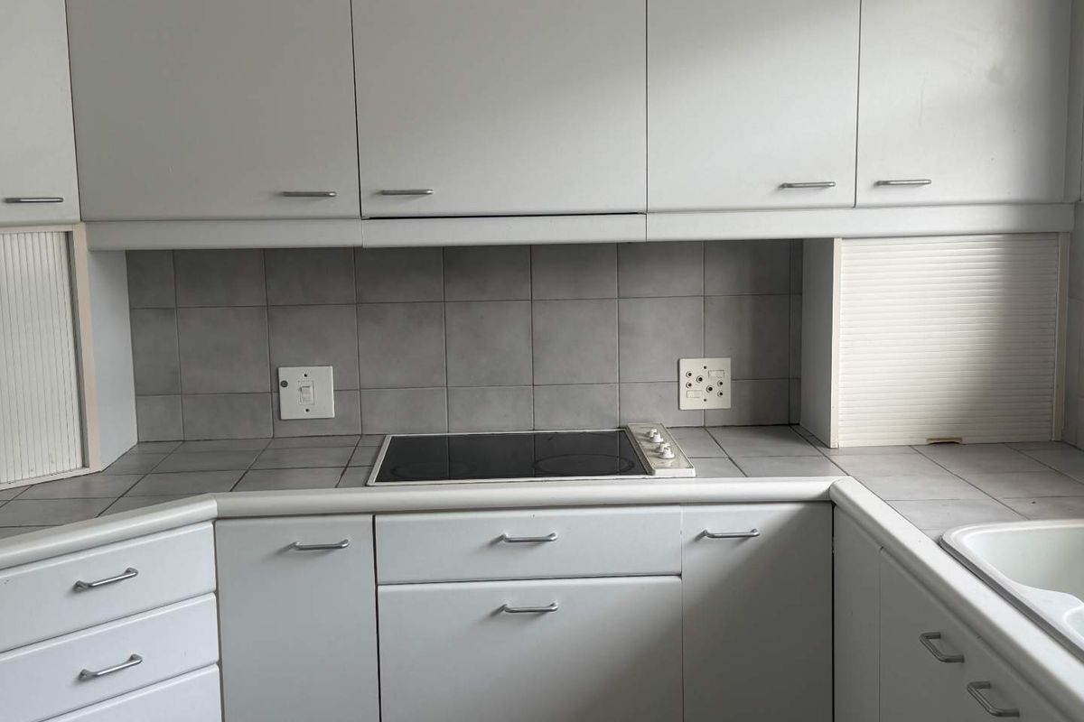 A functional kitchen featuring light-toned cabinetry, tiled countertops, and a built-in electric hob with a tiled backsplash.