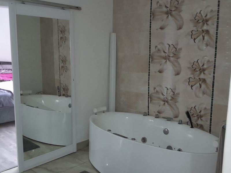 Bathroom featuring a modern freestanding jetted bathtub and decorative wall tiling, with a sliding mirror door providing access to the adjacent bedroom.