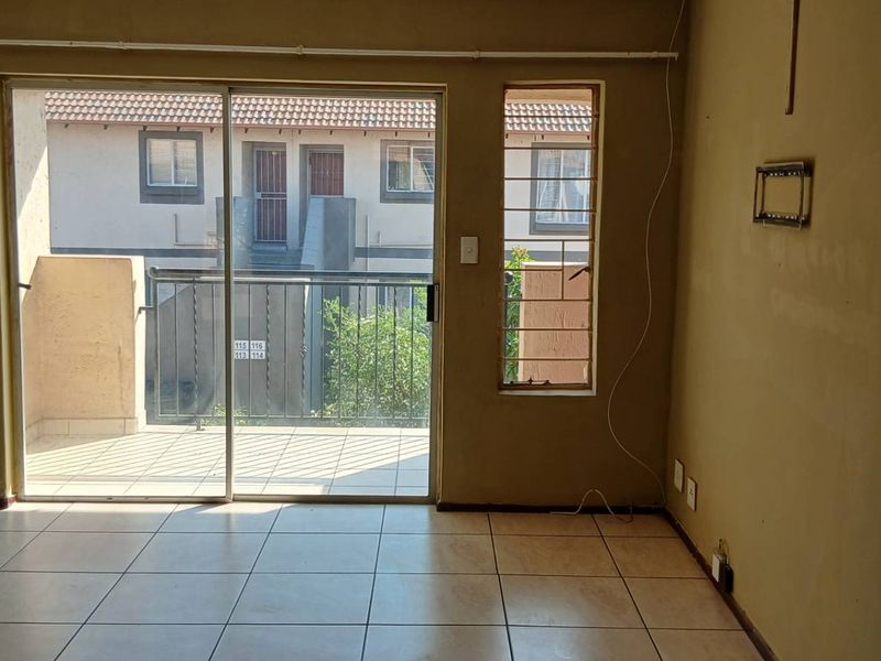 An empty living room featuring tiled floors and a sliding glass door leading to a balcony, requiring cosmetic updates to walls and finishes.