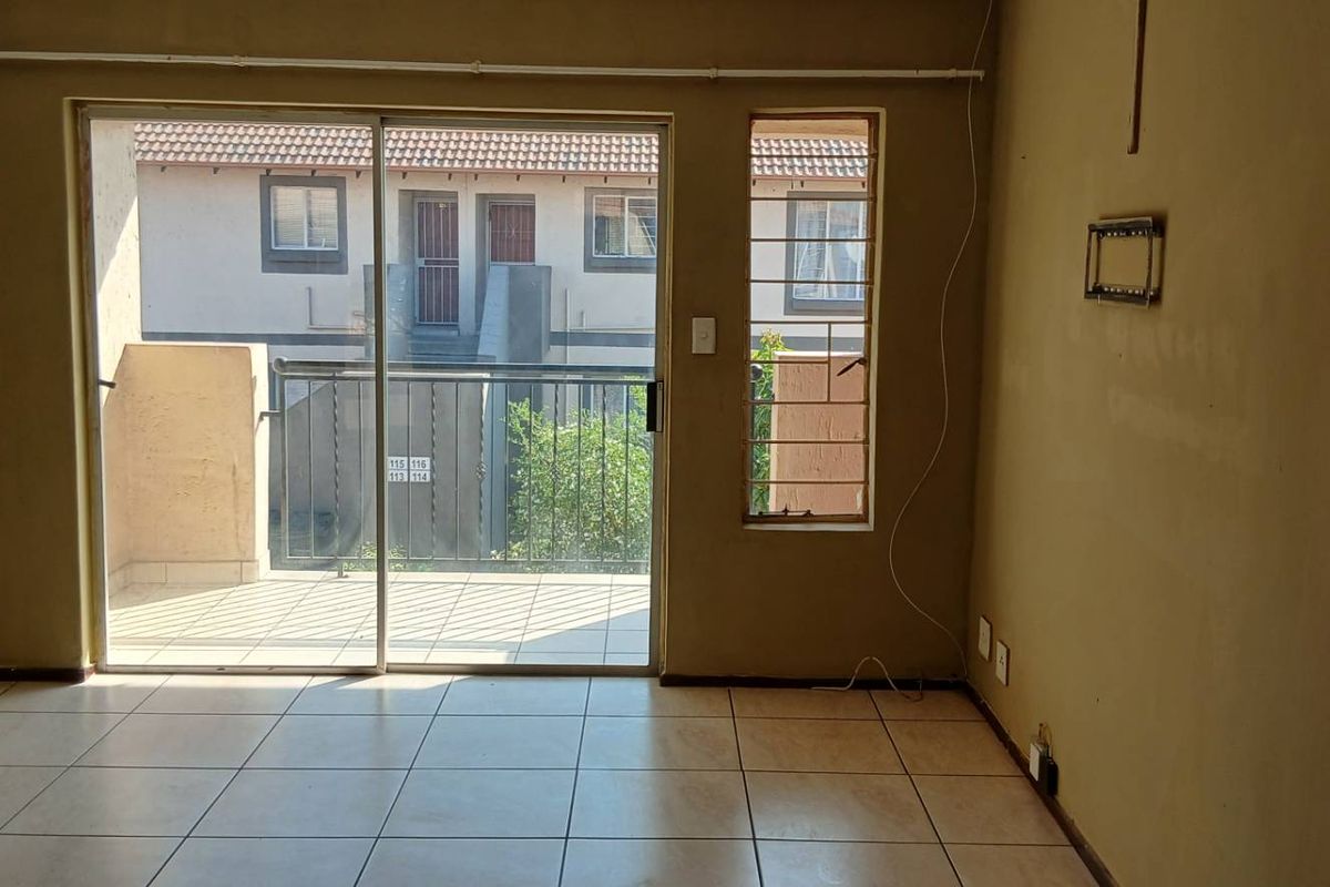 An empty living room featuring tiled floors and a sliding glass door leading to a balcony, requiring cosmetic updates to walls and finishes.