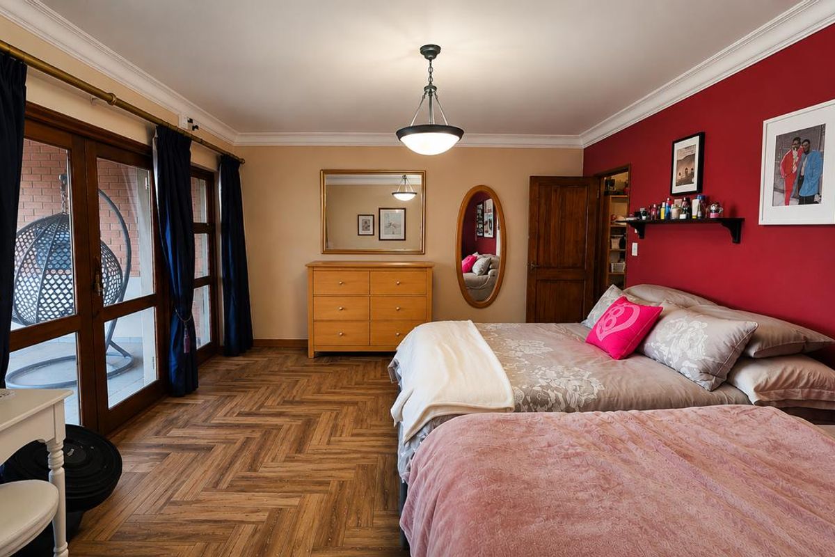 Spacious bedroom featuring herringbone wood-look flooring, a bold red accent wall, and large glass sliding doors providing direct access to the patio.