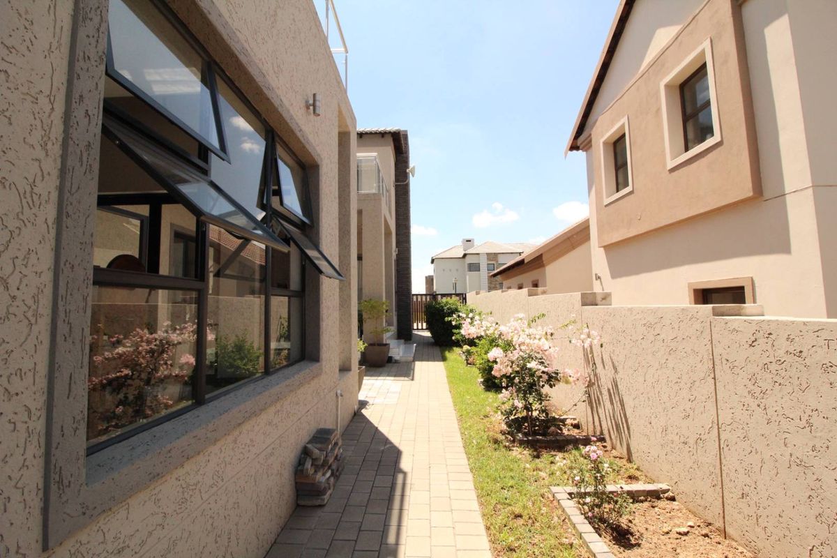 A side walkway featuring paved pathways, boundary walls, and landscaped garden beds alongside the property exterior.