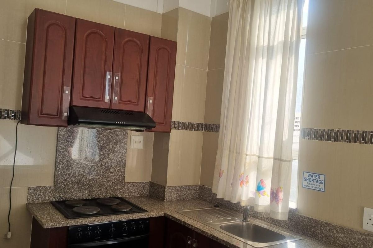 A functional kitchen featuring granite countertops, a built-in electric hob with extractor fan, and ample upper cabinetry with tiled wall finishes.