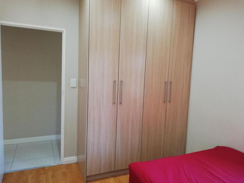 A bedroom featuring light wood-finish built-in wardrobes and laminate flooring, with an adjacent doorway leading to a tiled area.