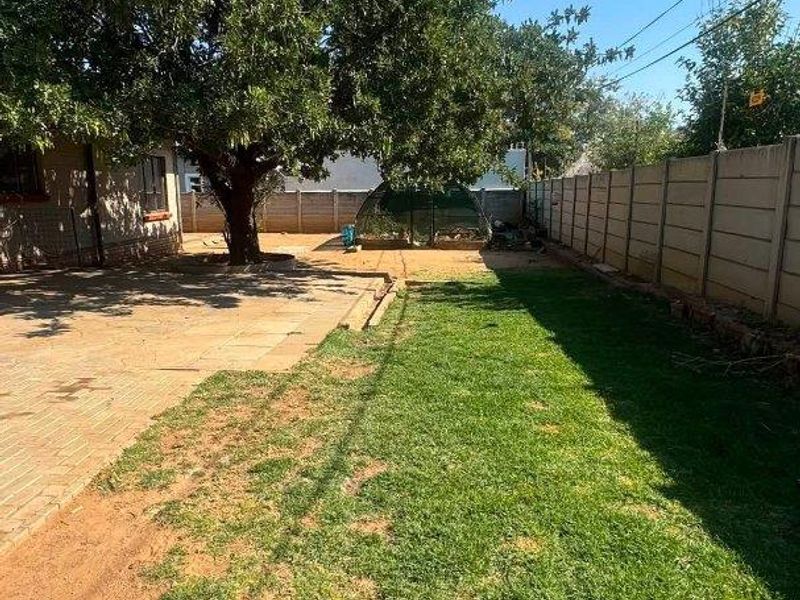 A rear garden featuring a paved patio area, a mature tree, and a lawn with perimeter precast concrete walling.