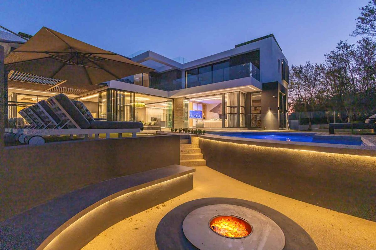 Modern luxury rear exterior featuring a swimming pool, sunken fire pit area, and seamless indoor-outdoor flow through large sliding glass doors.