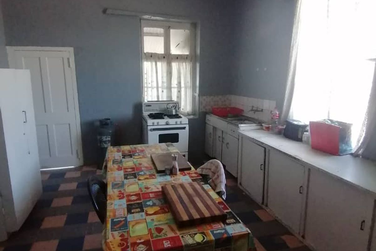 A dated kitchen featuring basic cabinetry, a freestanding stove, and a checkerboard tiled floor, offering significant potential for renovation and modernization.