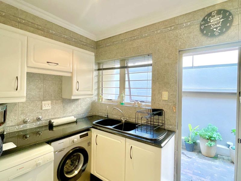 Functional scullery area featuring granite countertops, double basin sink, tiled splashbacks, and built-in cabinetry with direct access to an outdoor courtyard.