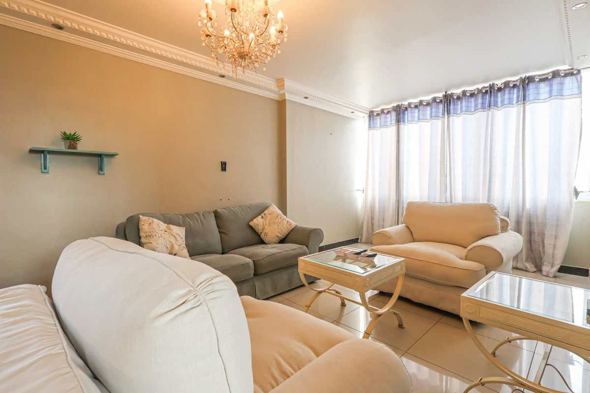 A comfortable living room featuring tiled flooring, decorative crown molding, and large windows that allow for ample natural light.