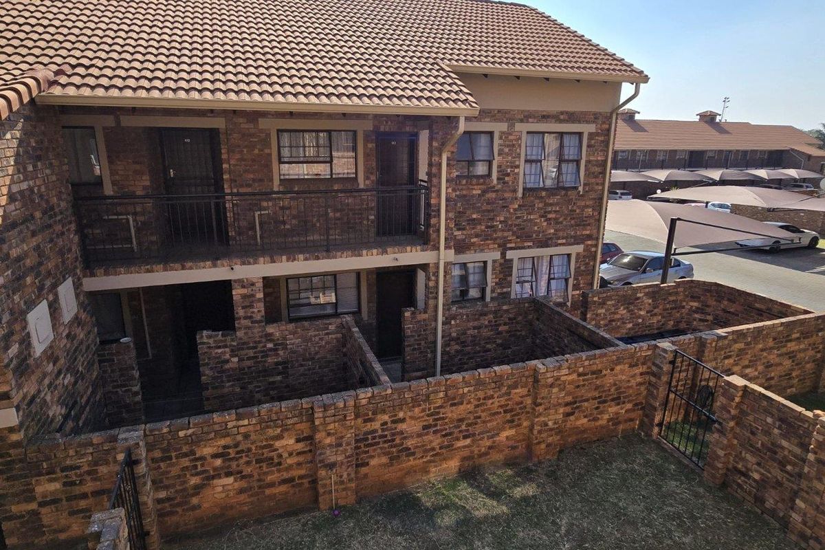Rear view of a multi-story apartment complex featuring face-brick construction, private ground-floor courtyards, and upper-level balconies.