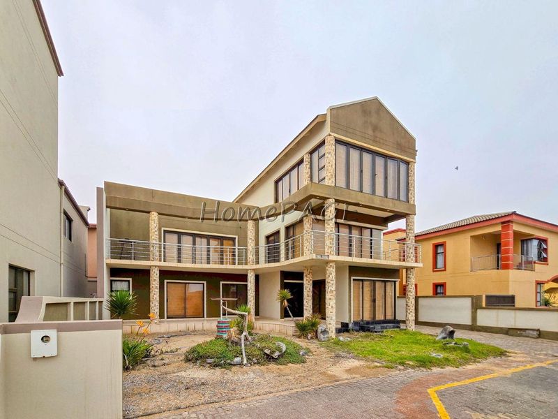 A multi-level residential property featuring stone-clad pillars, expansive balconies with stainless steel railings, and large sliding glass doors.
