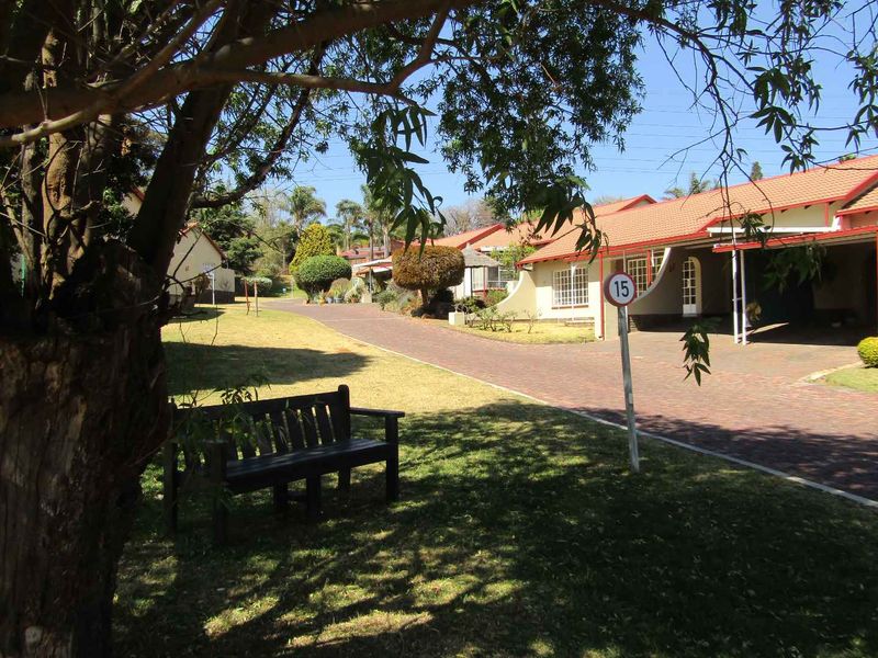A view of the retirement village grounds featuring paved driveways, established trees, and residential units with tiled roofs and carports.