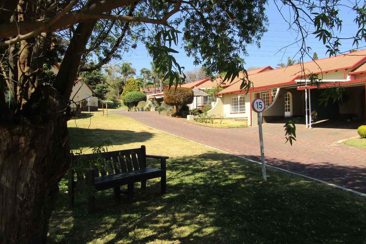A view of the retirement village grounds featuring paved driveways, established trees, and residential units with tiled roofs and carports.