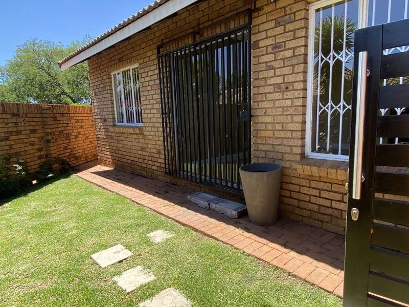 Rear exterior view of the townhouse featuring a face brick facade, secure metal gate, and a paved walkway leading to a private garden area.