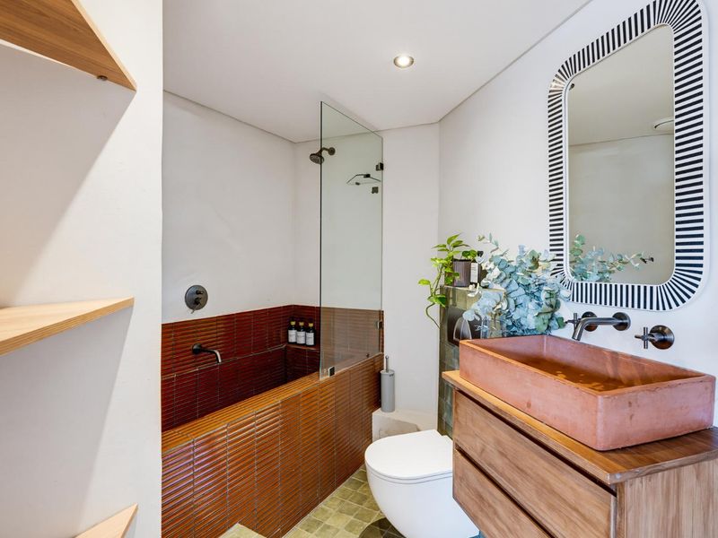 Modern bathroom featuring a tiled bathtub with glass screen, wall-hung toilet, and a custom wooden vanity with a unique vessel sink.