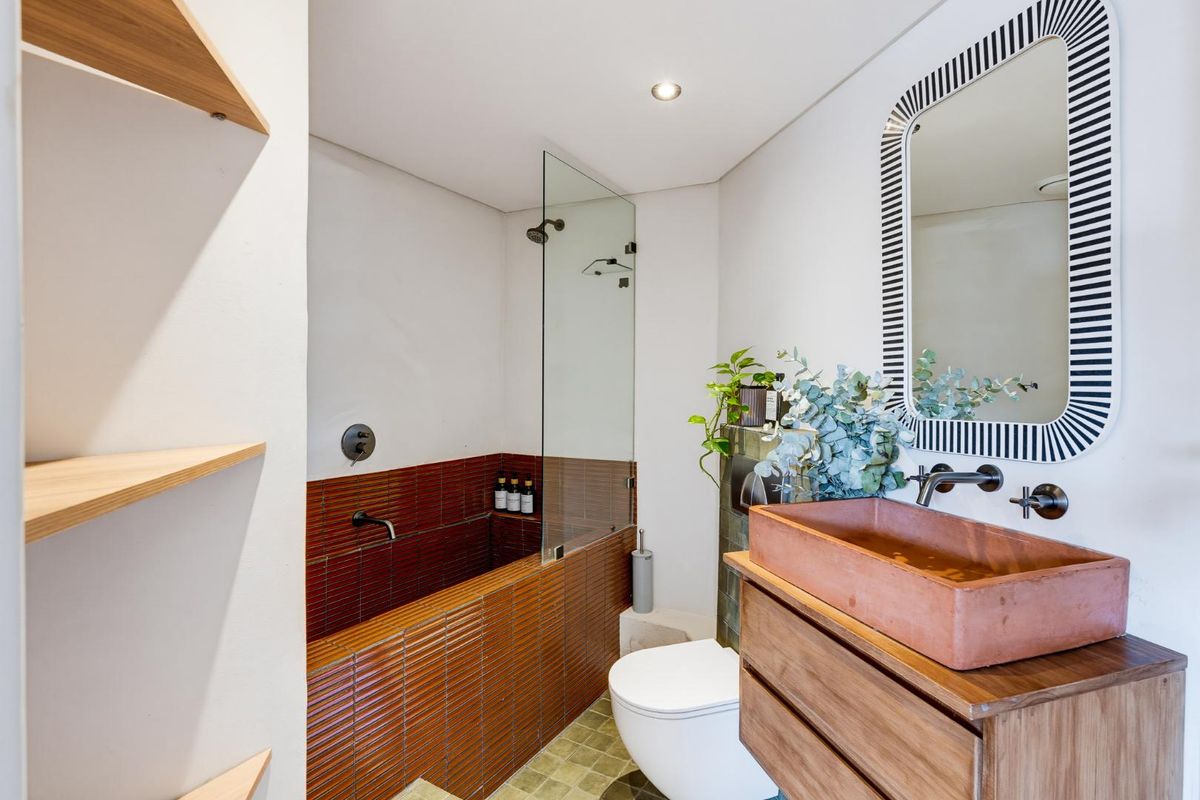 Modern bathroom featuring a tiled bathtub with glass screen, wall-hung toilet, and a custom wooden vanity with a unique vessel sink.