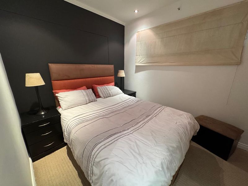 A cozy bedroom featuring a dark accent wall, recessed ceiling lighting, and a neutral roman blind.