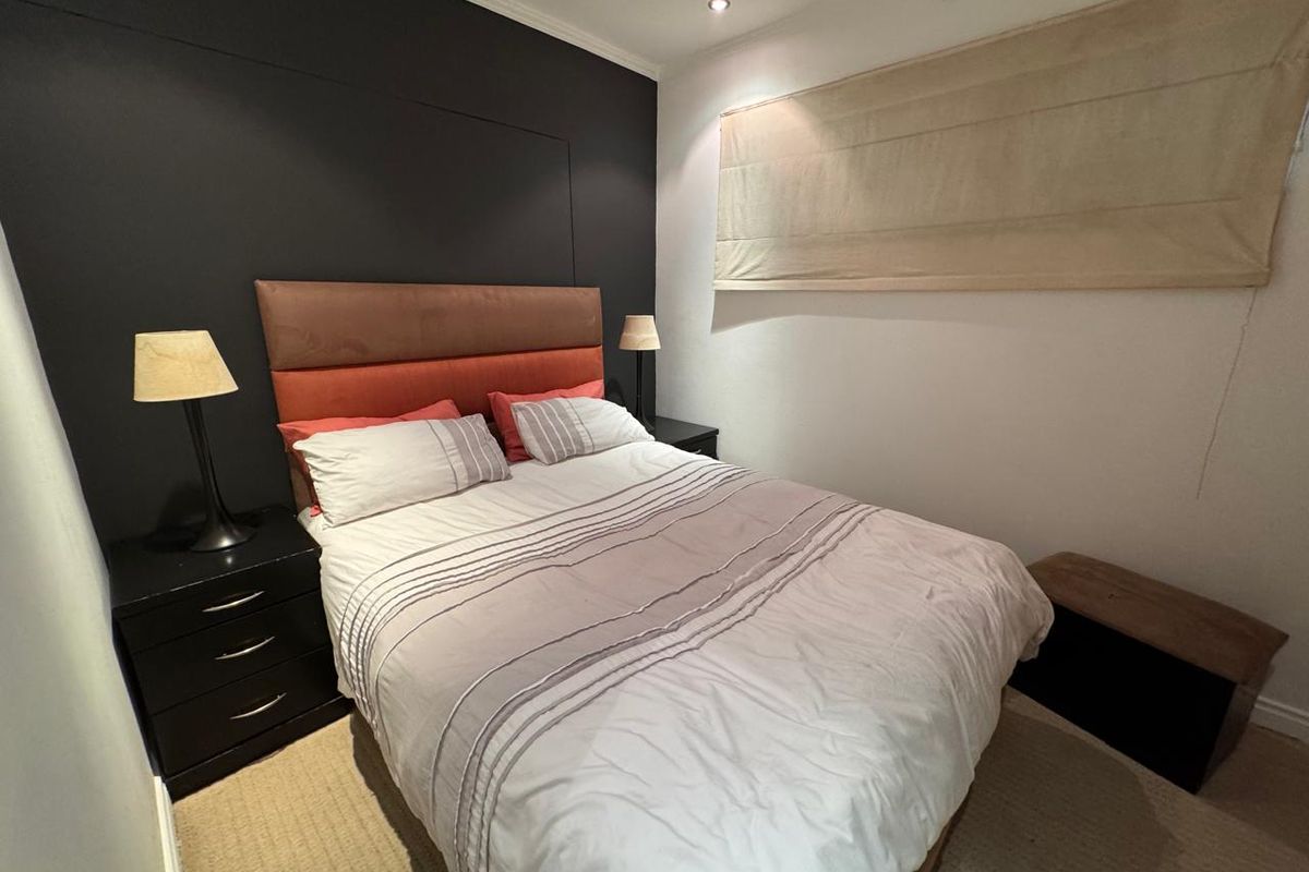 A cozy bedroom featuring a dark accent wall, recessed ceiling lighting, and a neutral roman blind.