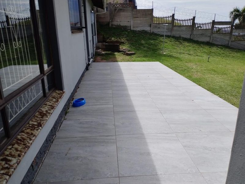 A paved outdoor patio area adjacent to the house, featuring tiled flooring and views of the rear garden and perimeter boundary wall.