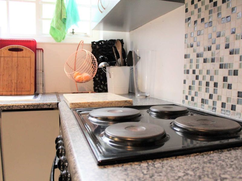 A functional kitchen area featuring a four-plate electric hob, granite countertops, and a decorative mosaic tile backsplash.
