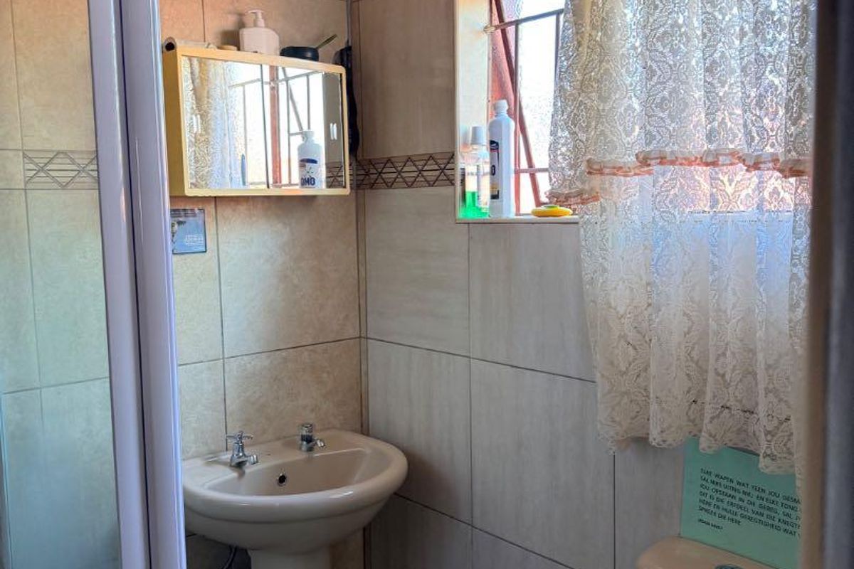 Compact bathroom featuring a pedestal basin, a shower enclosure with a glass door, and a standard toilet, finished with neutral wall tiles.