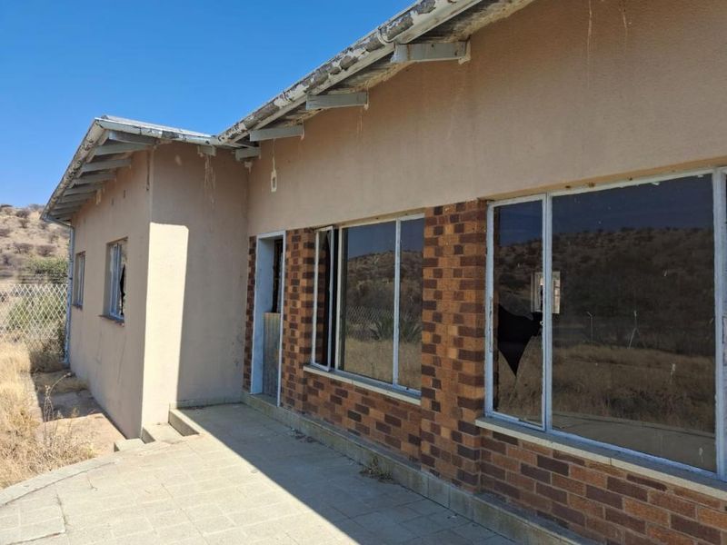 Rear exterior view of a residential property showing a paved patio, brick facade, and damaged window frames requiring maintenance and repair.